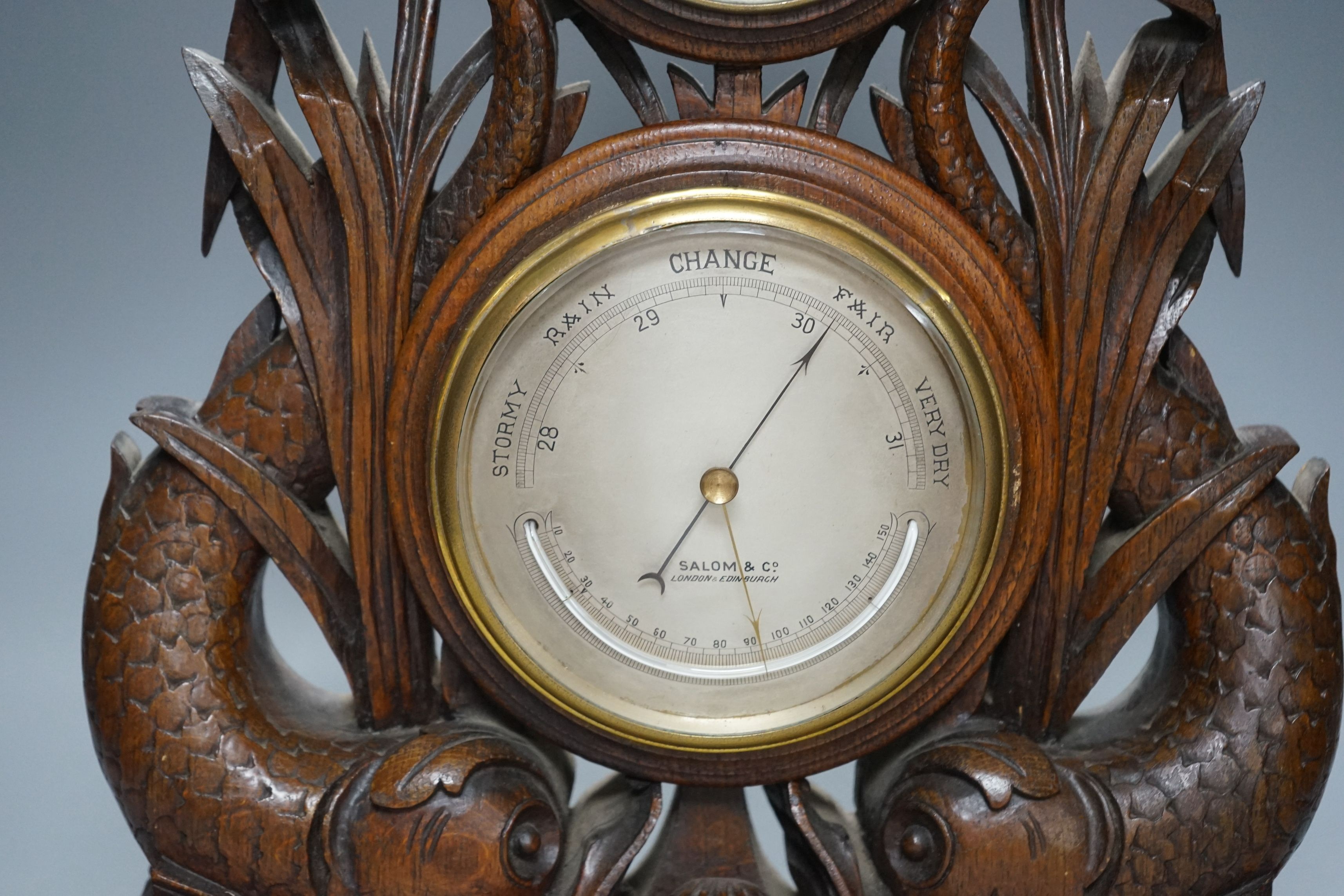 A Victorian oak timepiece combined barometer by Salom & Co., carved with stylised fish and bull rushes, height 46cm